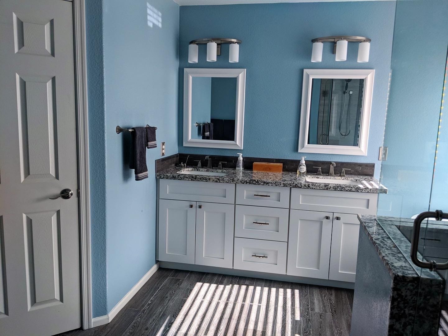 20220510_171529634_iOS Remodeled bathroom with double vanity, granite countertops, white cabinetry, and glass shower.