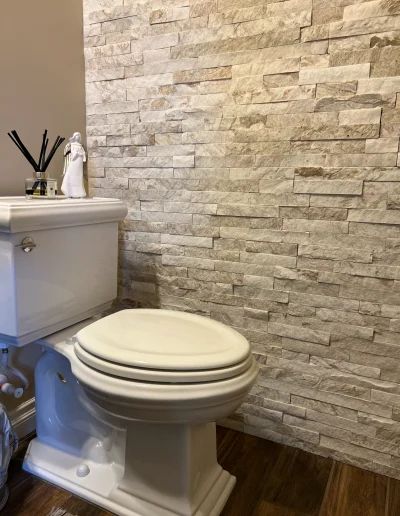 Bathroom remodel with white toilet and floor-to-ceiling stacked stone accent wall in neutral natural tones