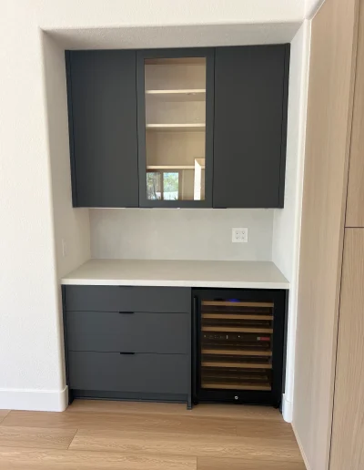 Remodeled dry bar with black cabinetry, white countertop, glass-front wine cooler, and mirrored upper cabinet