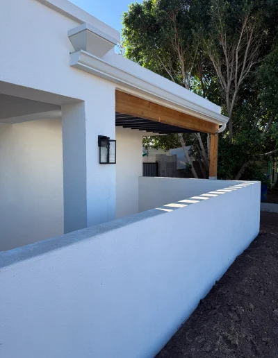 Remodeled home exterior with white stucco walls, wood patio framing, modern black wall light, rain gutter, and covered outdoor living area