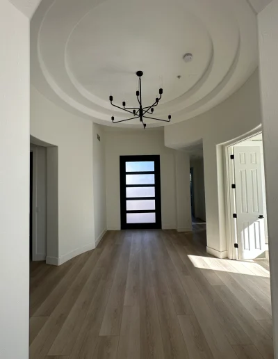Remodeled entryway with modern black front door, wood flooring, statement chandelier, and circular tray ceiling