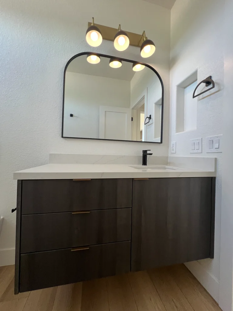 Modern guest bathroom remodel with dark wood vanity, white countertop, black fixtures, and arched mirror