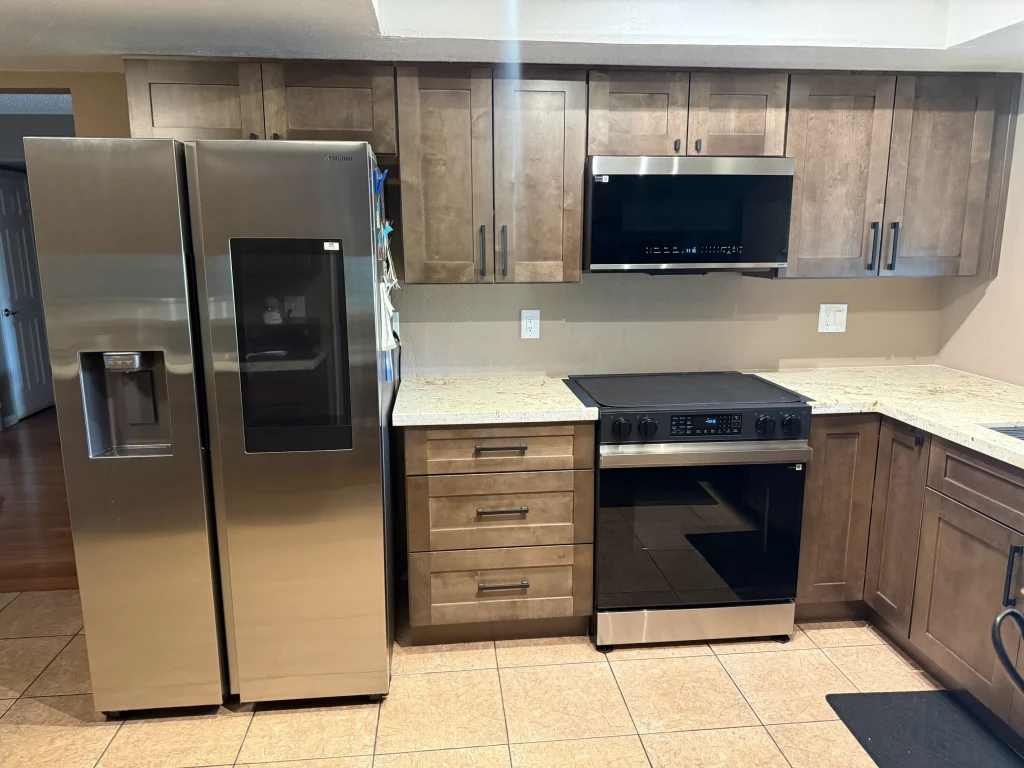 Remodeled kitchen with wood shaker cabinets, light stone countertops, stainless steel appliances, and modern black cabinet hardware