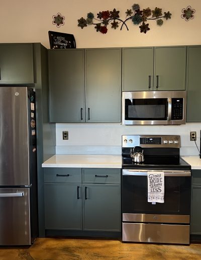 Remodeled kitchen with green shaker cabinets, white countertops, black hardware, and stainless steel appliances