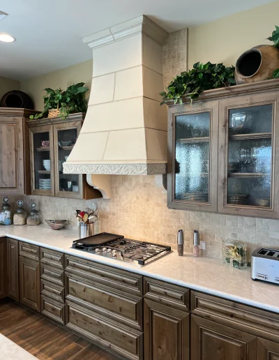 Custom kitchen with rustic wood cabinetry, stone tile backsplash, quartz countertops, gas cooktop, and decorative vent hood