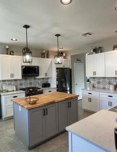 Kitchen remodel with white shaker cabinets, gray island with butcher block countertop, patterned tile backsplash, pendant lighting, and stainless steel appliances