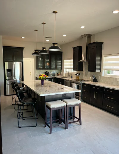 Remodeled kitchen with dark wood cabinetry, oversized stone island, pendant lighting, stainless steel appliances, and light tile flooring