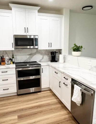 Modern kitchen remodel with white shaker cabinets, marble-look countertops and backsplash, stainless steel appliances, and wood-look flooring