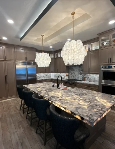 Luxury kitchen remodel with custom cabinetry, oversized stone island, pendant lighting, stainless steel appliances, and wood-look flooring