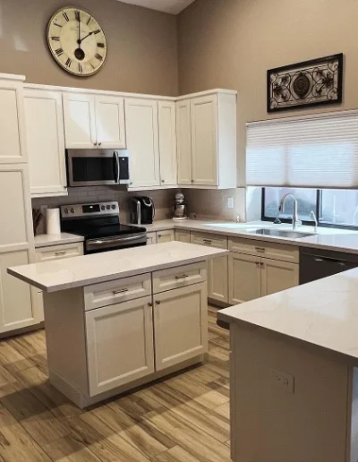 Bright remodeled kitchen with white cabinetry, quartz countertops, center island, tile backsplash, and wood-look flooring