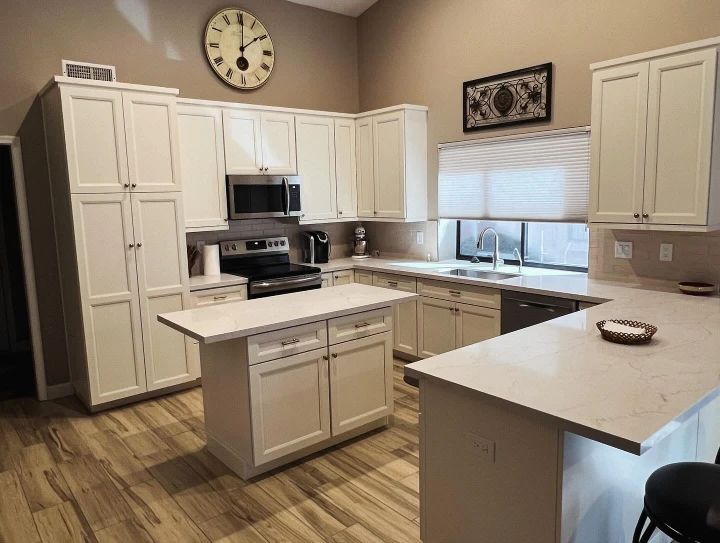 Bright remodeled kitchen with white cabinetry, quartz countertops, center island, tile backsplash, and wood-look flooring