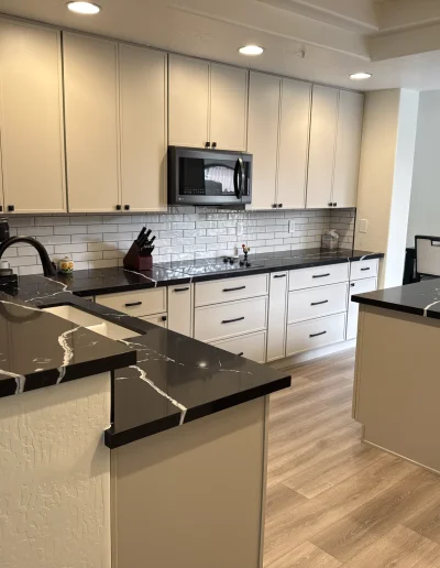 Full kitchen remodel with white cabinetry, black quartz countertops, subway tile backsplash, and large center island
