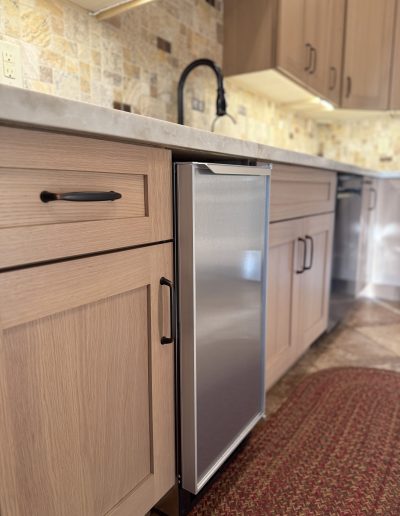 Full kitchen remodel featuring natural wood shaker cabinets, stone countertops, tile backsplash, black faucet, and stainless steel dishwasher