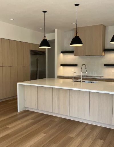 Modern kitchen remodel with light wood cabinetry, large white island, black pendant lights, and stainless steel appliances
