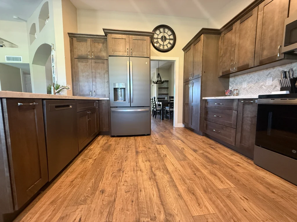 Full kitchen remodel with dark wood cabinetry, stainless steel appliances, herringbone backsplash, and wood-look flooring