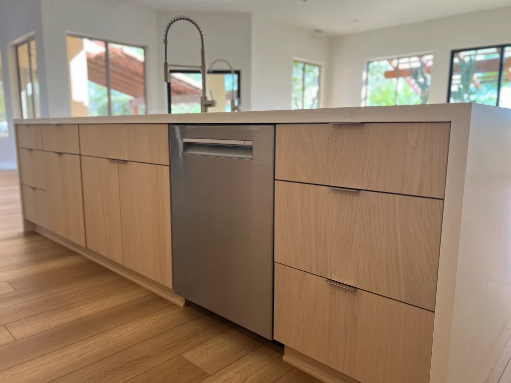 Custom kitchen island with light wood cabinetry, white quartz countertop, stainless steel dishwasher, and wood flooring