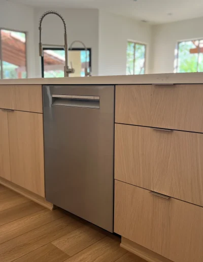Custom kitchen island with light wood cabinetry, white quartz countertop, stainless steel dishwasher, and wood flooring