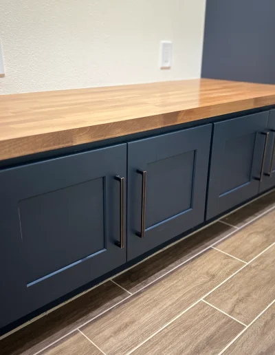 Remodeled laundry room with navy blue shaker cabinets, butcher block countertop, black hardware, and wood-look tile flooring