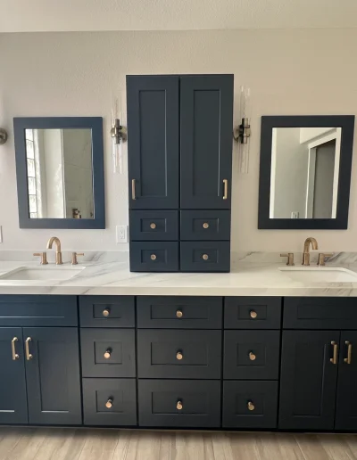 Primary bathroom remodel with dark blue double vanity, marble-look countertop, brass fixtures, framed mirrors, and matching built-in storage