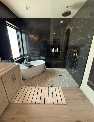 Luxury master bathroom remodel with freestanding soaking tub, walk-in glass shower, black marble-look wall tile, and rainfall showerhead