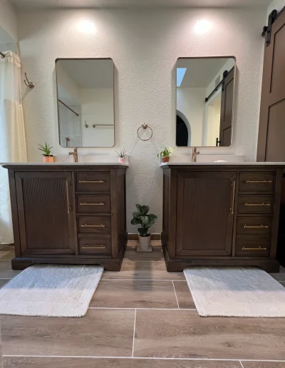 Primary bathroom remodel with two dark wood vanities, brass hardware, modern mirrors, and tile flooring