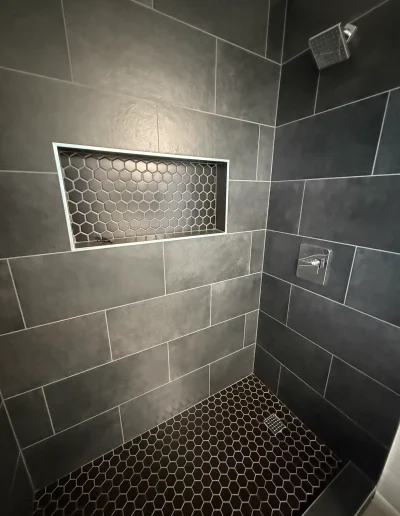 Modern walk-in shower with dark gray large-format wall tile, hexagon mosaic floor tile, built-in shower niche, and square rainfall showerhead