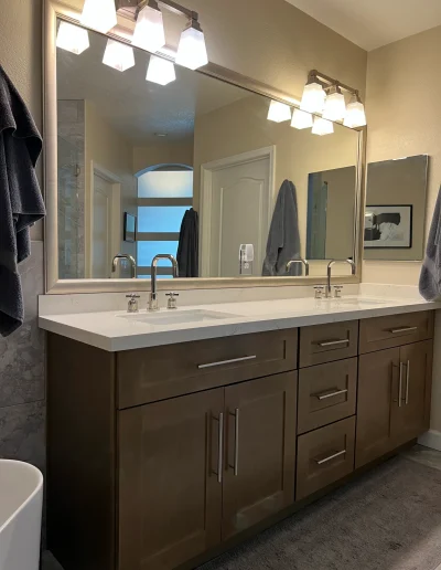 Remodeled master bathroom with double sink vanity, wood cabinetry, quartz countertop, large framed mirror, and modern vanity lighting