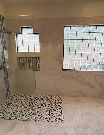 Primary bathroom remodel with frameless glass walk-in shower, marble-look tile, pebble shower floor, and built-in niche