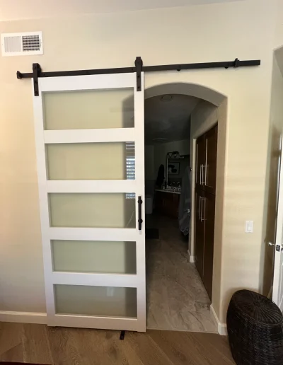 White sliding barn door with frosted glass panels and black hardware leading to a remodeled master bathroom