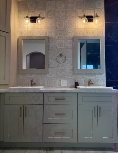 Custom double bathroom vanity with taupe shaker cabinets, quartz countertop, decorative patterned tile backsplash, and brass fixtures