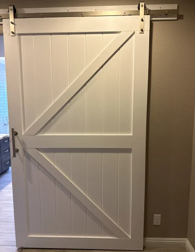 White farmhouse-style sliding barn door with diagonal panel detailing, metal track, and modern pull handle
