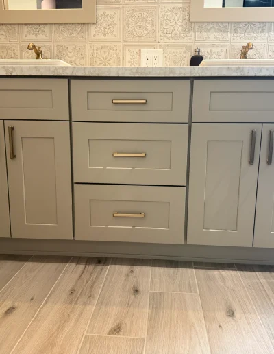 Custom master bathroom double vanity with shaker cabinetry, quartz countertop, brushed brass hardware, and wood-look tile flooring