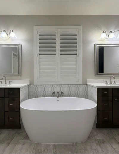 Primary bathroom remodel with freestanding soaking tub, dual dark wood vanities, white countertops, and geometric tile backsplash