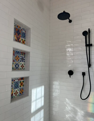 Walk-in shower with white subway tile, colorful decorative tile niches, matte black rain showerhead, and handheld shower fixture