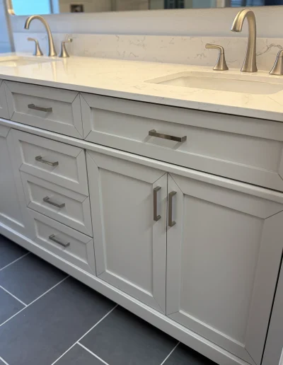 Primary bathroom remodel with gray double vanity, white quartz countertop, undermount sinks, brushed nickel faucets, and dark tile flooring