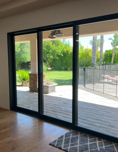 Large black framed multislide glass door opening to a covered patio, green lawn, and landscaped backyard