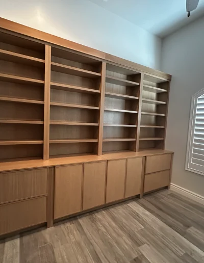 Custom home office built-in with floor-to-ceiling wood shelving, integrated lower cabinets and drawers, and wood-look flooring