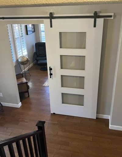 Home office remodel with modern white sliding barn door featuring glass panels, wood flooring, and gray painted walls