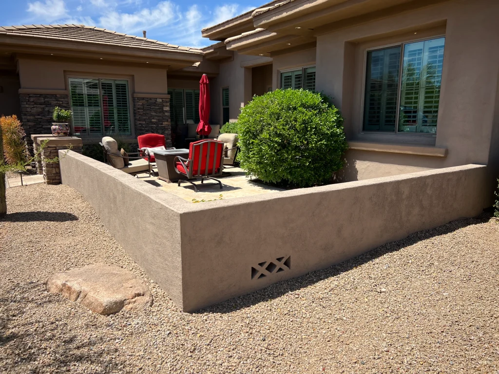 Remodeled outdoor patio with stucco pony wall, seating area, desert landscaping, and stone accents