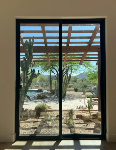 Black framed sliding glass door overlooking a desert backyard with cacti, pergola, and mountain views