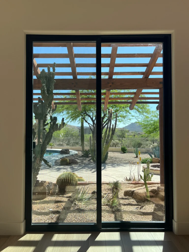 Black framed sliding glass door overlooking a desert backyard with cacti, pergola, and mountain views