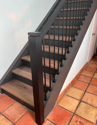Remodeled interior staircase with wood-look stair treads, dark risers, black railing, square newel post, and metal balusters