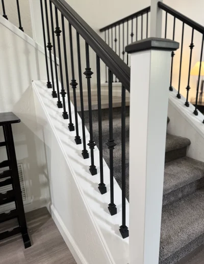 Remodeled staircase with gray carpet, white trim, black iron balusters, and dark wood handrail