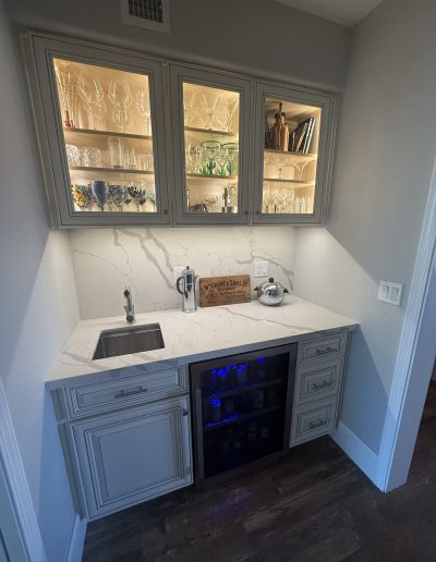 Custom wet bar with illuminated glass-front cabinets, quartz countertop and backsplash, undermount sink, beverage refrigerator, and built-in cabinetry