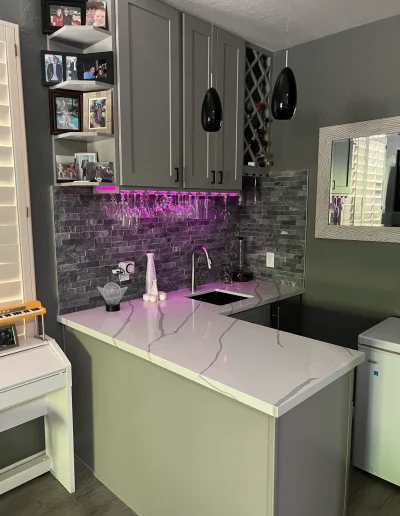 Custom wet bar with gray cabinetry, white quartz countertop, stone tile backsplash, wine storage, sink, and under-cabinet lighting