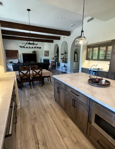 Open-concept home remodel featuring custom wood kitchen cabinetry, large stone island, wood-look flooring, exposed ceiling beams, and adjoining living area